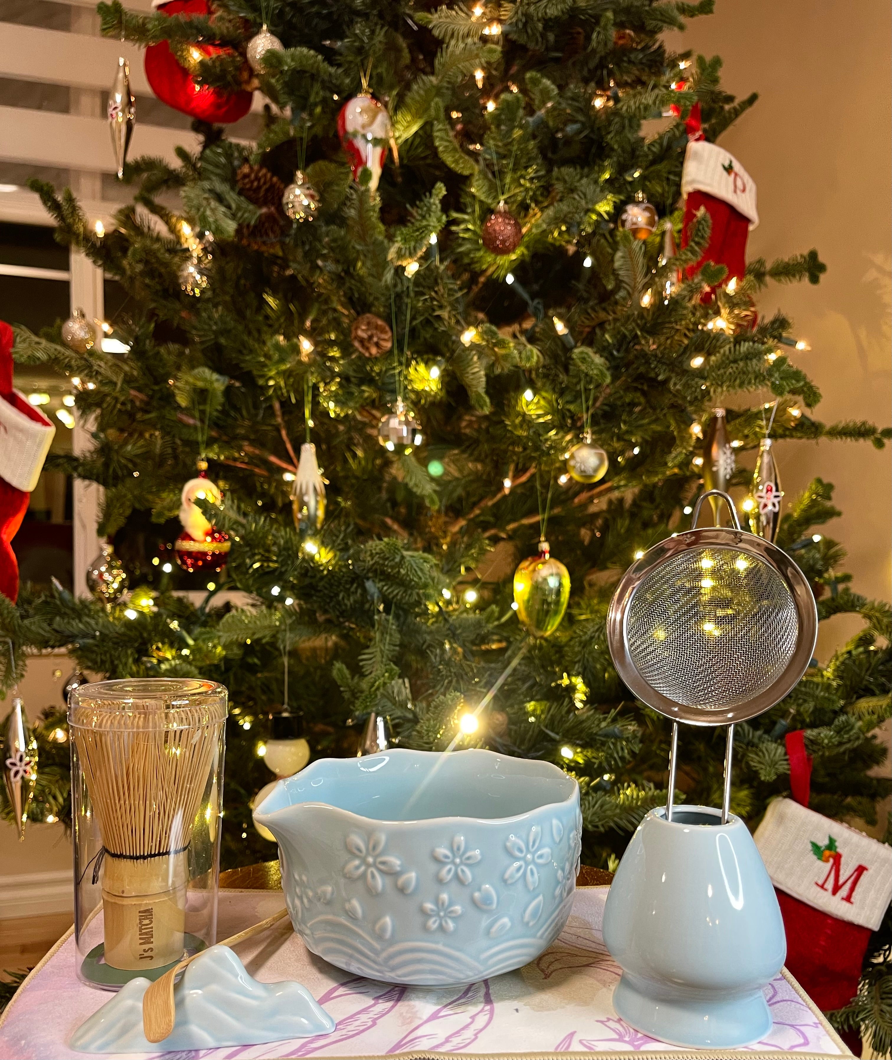 Decorative items on a table in front of a Christmas tree with lights.
