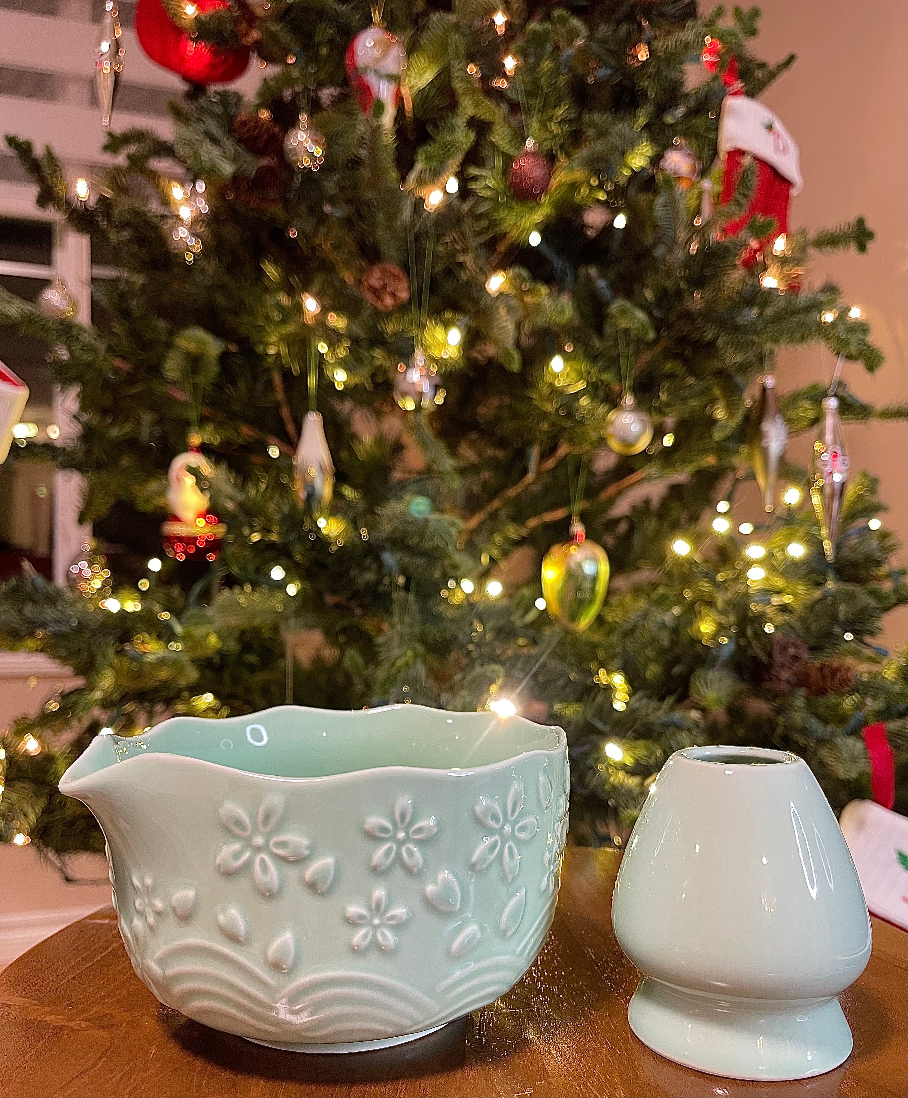 Two ceramic containers on a table with a decorated Christmas tree in the background.