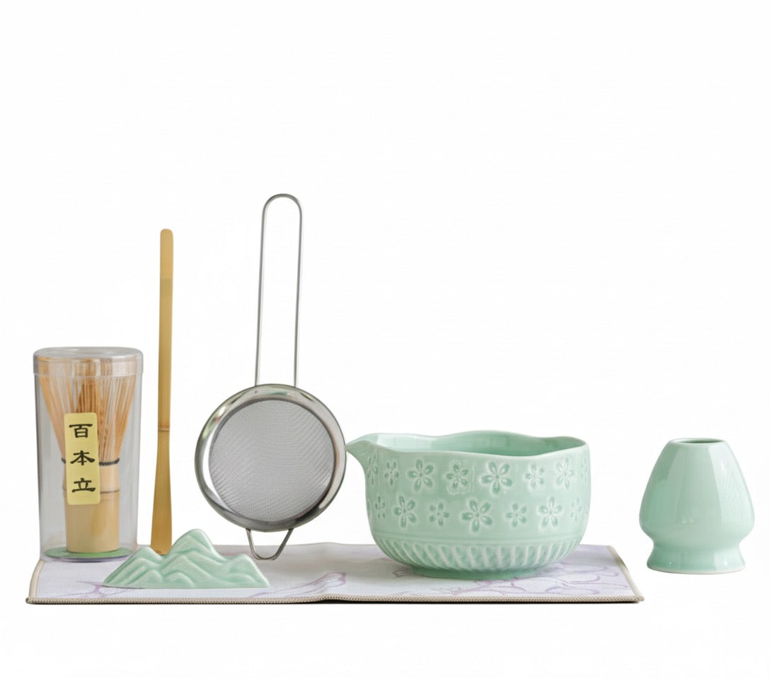 Set of green ceramic tea accessories including a bowl, strainer, and other items on a white background